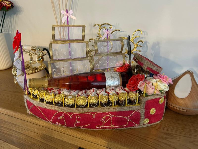 Handgebautes Geschenkschiff mit Segeln, Rumpf aus rotem Stoff, Ferrero Rocher, Raffaello und Roséwein